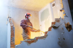 worker with sledgehammer at indoor wall destroying