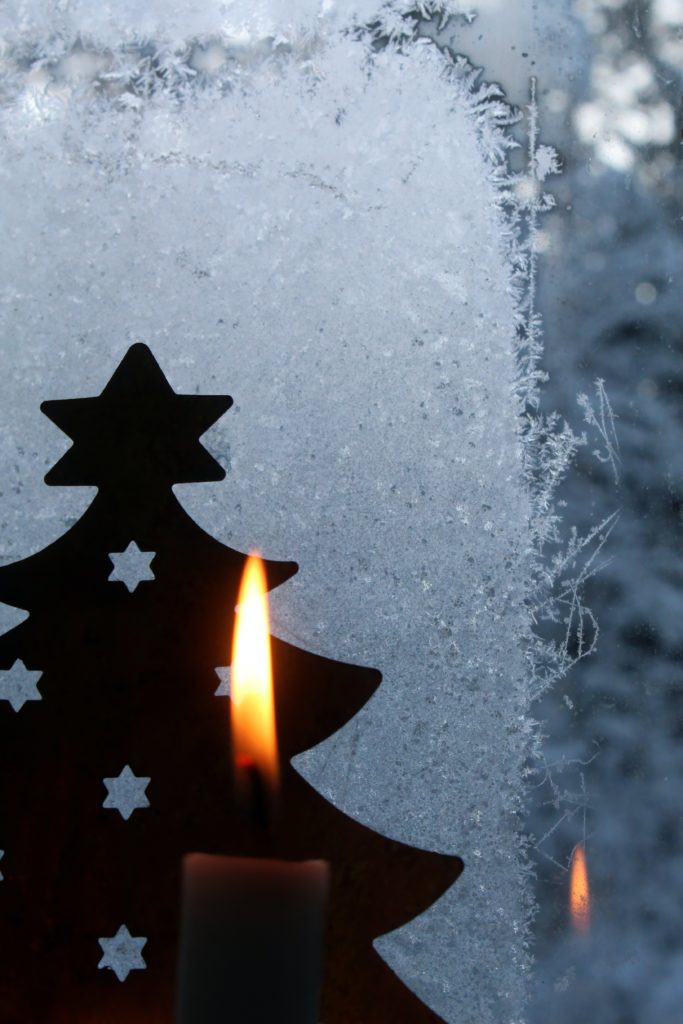 A candle flame in front of a metal tree decoration.
